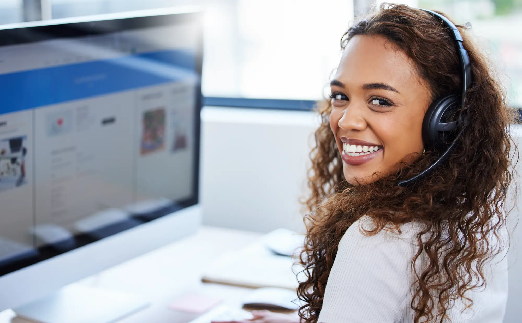 Analista de atendimento sorrindo, com headset, diante do computador com a plataforma aberta